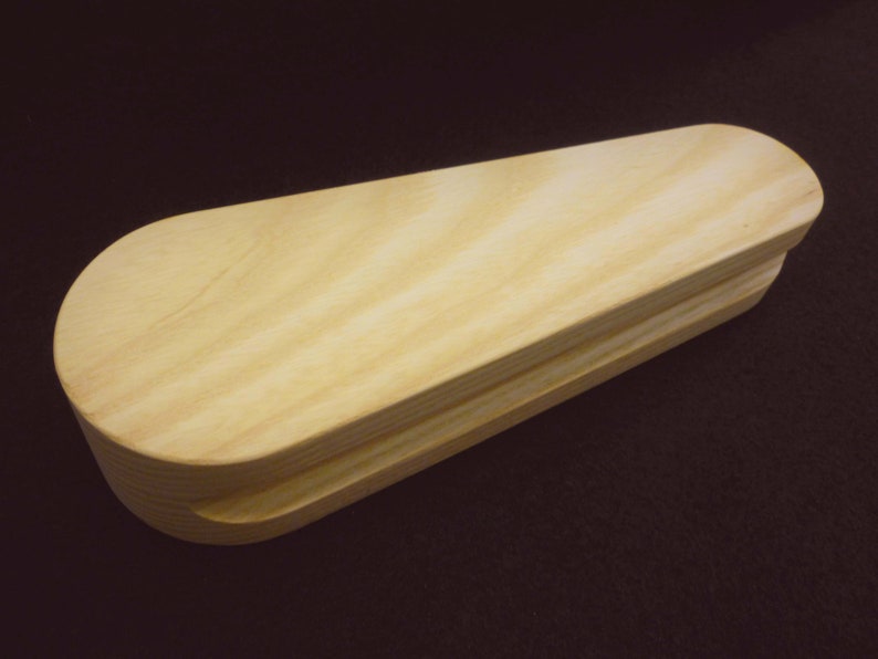 May include: A wooden box with a rounded top and a smooth, light brown finish. The box is made of two pieces of wood that are joined together.