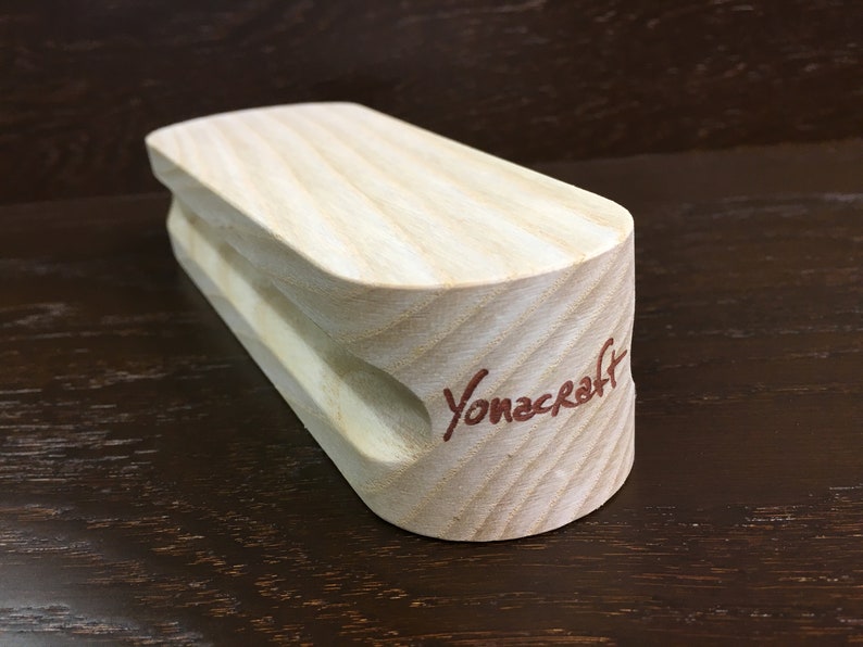 May include: A light wood climbing hold with a rounded shape and a small hole in the center. The hold is branded with the text "Yonacraft" in red.
