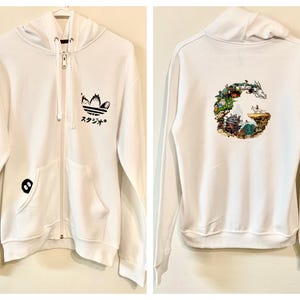 May include: White zip-up hoodie with a Studio Ghibli logo on the back and an Adidas logo on the front. The sleeves have the text "スタジオジブリ" in blue.