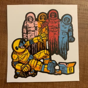 May include: A yellow Pac-Man character wearing a space suit and holding a box that says "Anti Anxiety 6 Pac".  Four ghost characters in pink, orange, red, and blue are in the background.