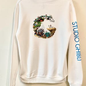 May include: White hoodie with a graphic of a G made up of Studio Ghibli characters and scenes. The right sleeve has the text "STUDIO GHIBLI" printed in blue.