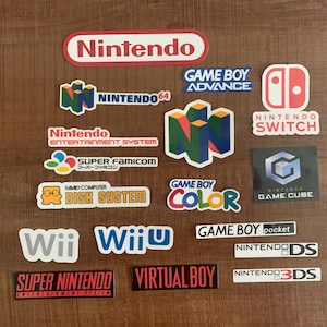 May include: A collection of Nintendo stickers featuring logos for various gaming consoles, including Nintendo, Game Boy, Wii, and Nintendo Switch. The stickers are in various colors and designs, with the Nintendo logo prominently displayed.