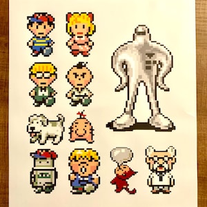 Puede incluir: Un conjunto de 10 pegatinas de arte de píxeles con personajes del videojuego Earthbound. Las pegatinas están impresas en papel blanco e incluyen un perro blanco, un robot rojo y blanco, una criatura roja con un globo de diálogo, un hombre con gafas y una bata de laboratorio blanca, un hombre con una camisa azul y una gorra de béisbol, un hombre con una camisa amarilla y una gorra de béisbol, un hombre con una camisa amarilla y una corbata de lazo roja, un bebé con un lazo rojo, una niña con un vestido rosa y cabello amarillo, y una figura humanoide blanca.