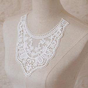 May include: A white lace collar with a floral and geometric design. The collar is displayed on a mannequin and features a scalloped edge. The delicate lace is semi-transparent, revealing the mannequin beneath. This item is suitable for sewing and craft projects.
