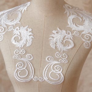 Può includere: Applicazione in pizzo bianco ricamato con un delicato motivo floreale e a spirale. L'applicazione è esposta su un manichino, mostrando gli intricati dettagli del pizzo. Perfetta per abiti da sposa o altri progetti artigianali.