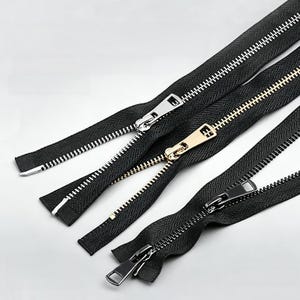 May include: Three black fabric zips with metal teeth and sliders. The first zip has silver-tone teeth and a silver slider, the second has gold-tone teeth and a gold slider, and the third has dark gunmetal-tone teeth and a matching dark slider.