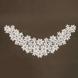May include: A white lace collar applique featuring a repeating floral pattern with interconnected petals. The design is curved in a crescent shape, composed of multiple small and large flower motifs linked together to form a decorative neckline.