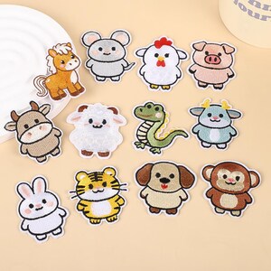Puede incluir: Un conjunto de doce parches bordados termoadhesivos con animales de dibujos animados, incluyendo un caballo, ratón, pollo, cerdo, vaca, oveja, dragón, cabra, conejo, tigre, perro y mono, cada uno con un borde blanco y costuras detalladas.