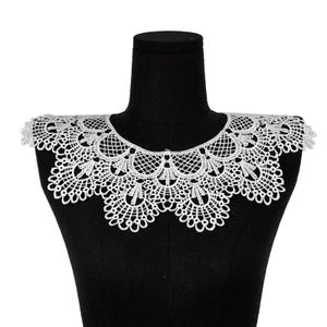 May include: A white lace collar featuring an intricate scalloped edge and a detailed floral-inspired openwork pattern. The accessory has a rounded neckline and a wide, decorative design that extends across the shoulders with a delicate finish.
