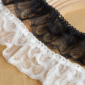 Peut inclure: Gros plan sur deux garnitures en dentelle, une blanche et une noire. La dentelle a un bord festonné et un motif délicat en forme de fleur. Les garnitures sont froncées, ajoutant de la texture et de la dimension au design. Idéal pour la couture et les projets d'artisanat.