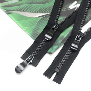 May include: Two black zippers with large, chunky teeth and matching black pull tabs. The zippers feature a sturdy fabric tape and a smooth, glossy finish on the metal sliders, designed for heavy-duty fastening applications on various garments.