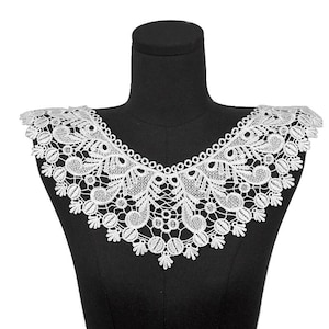 May include: A white lace collar featuring an intricate floral and scrollwork pattern with scalloped edges. The lace is constructed with a dense, interconnected thread design that forms a wide, decorative neckline piece with a pointed center.