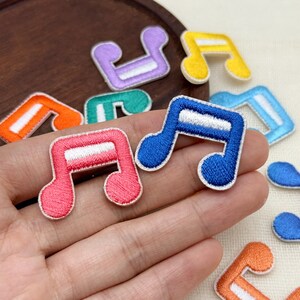 May include: A collection of embroidered musical note patches in various colors including pink, blue, orange, purple, green, yellow, and light blue. Each patch features a white horizontal stripe across the center of the note symbol.