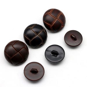 May include: A collection of five round buttons in varying sizes, featuring a dark brown color and a textured, woven-look surface pattern. Three buttons are displayed face-up, while two smaller buttons are flipped to show the back shank attachment.