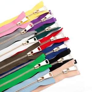 May include: A collection of eleven fabric zippers arranged in a fan pattern, featuring a variety of colors including yellow, pink, purple, dark green, gray, white, red, blue, brown, black, light green, light blue, and beige with gold metal pulls.
