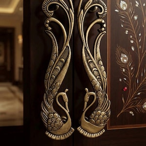 May include: A pair of antique brass door handles shaped like stylized peacocks with intricate feather detailing, mounted on a dark wood door featuring inlaid mother-of-pearl peacock feather patterns and scattered white jasmine flowers.