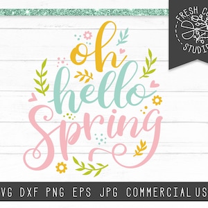 Puede incluir: Un diseño digital con el texto "oh hello spring" en letras rosa, amarillo y azul con hojas y flores verdes. El diseño está sobre un fondo de madera blanca.