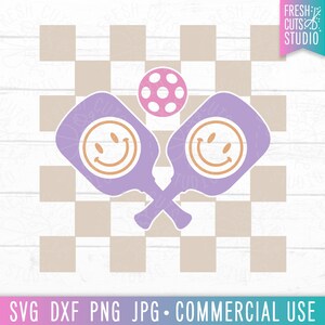 May include: Two purple paddles with smiley faces on a checkered background. A pink and white ball is in the center of the paddles.