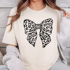 May include: A white t-shirt with a black and white leopard print bow design.