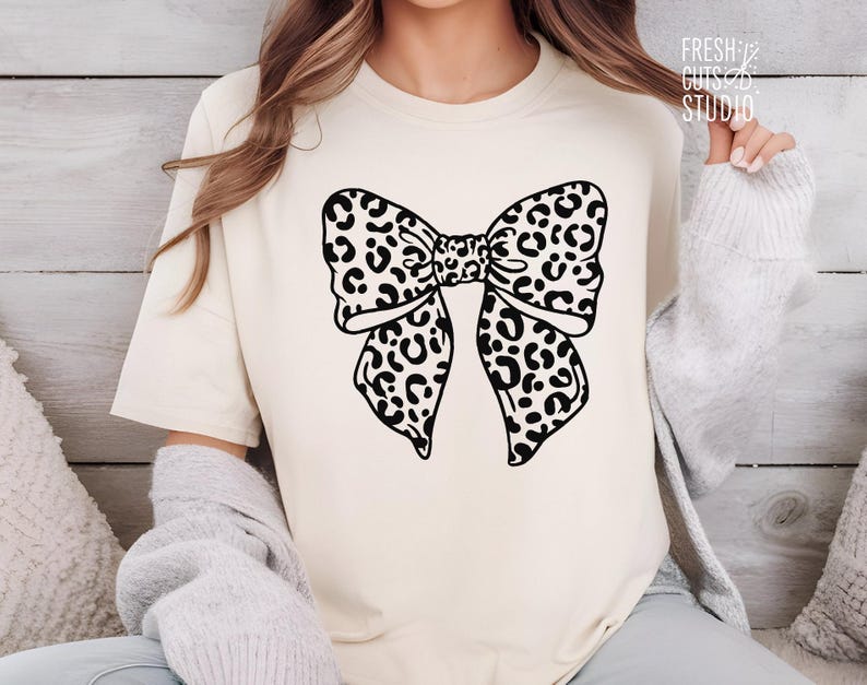 May include: A white t-shirt with a black and white leopard print bow design.