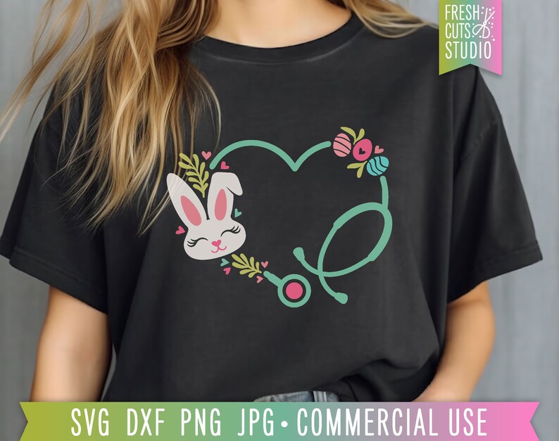 May include: A black t-shirt with a green stethoscope design in the shape of a heart. A pink and white bunny with pink ears is inside the heart. The bunny has pink eyes and a pink nose. The design is surrounded by pink and green flowers and hearts.