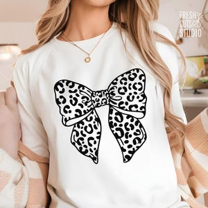 May include: White sweatshirt with a black and white leopard print bow design.