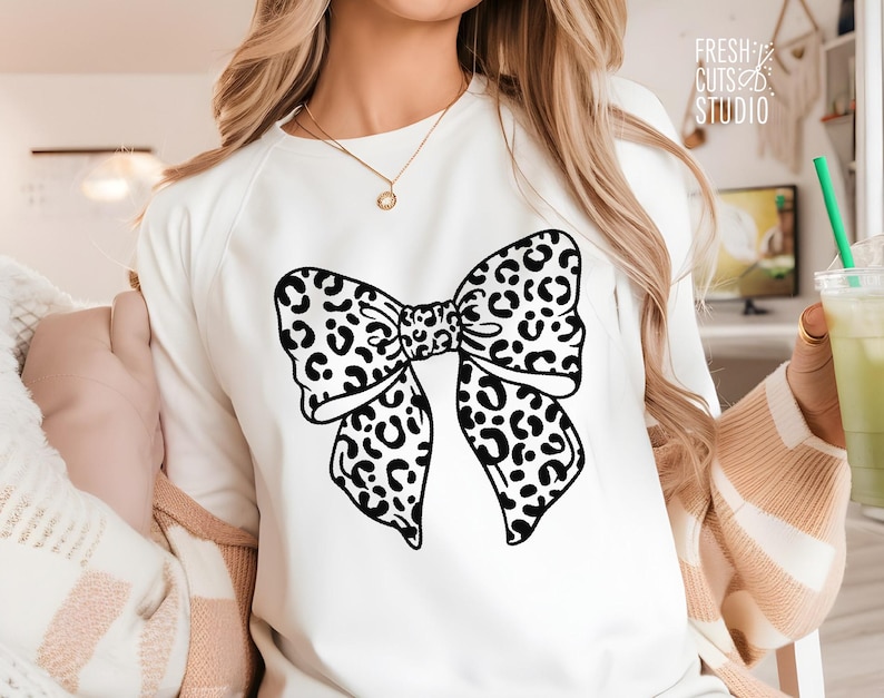 May include: White sweatshirt with a black and white leopard print bow design.