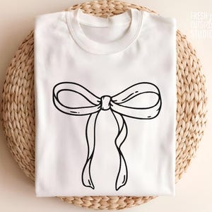 May include: A white t-shirt with a black outline of a bow on the front.