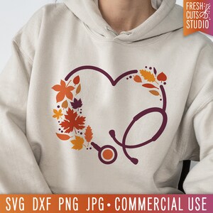 Op de afbeelding: Een beige hoodie met een donkerrode stethoscoop in de vorm van een hart. Het hart is gevuld met oranje, rode en bruine herfstbladeren.