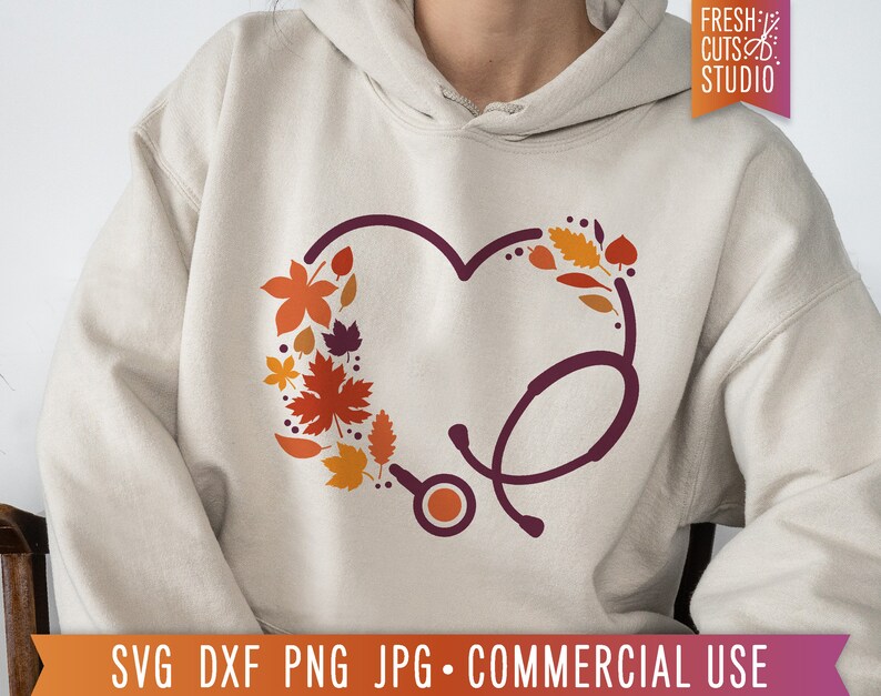 Op de afbeelding: Een beige hoodie met een donkerrode stethoscoop in de vorm van een hart. Het hart is gevuld met oranje, rode en bruine herfstbladeren.