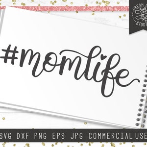 May include: A black and white graphic design with the text "#momlife" in a cursive font. The text includes a small heart symbol.