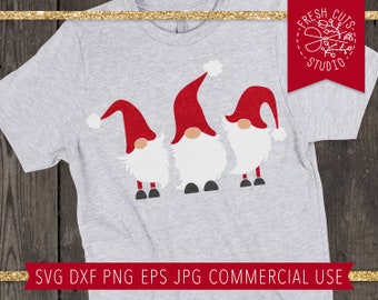 Könnte beinhalten: Ein hellgraues T-Shirt mit einer Grafik von drei Wichteln. Jeder Wichtel hat einen roten Hut mit einem weißen Bommel, einen großen weißen Bart und schwarze Schuhe. Der Text "SVG DXF PNG EPS JPG COMMERCIAL USE" steht unten.
