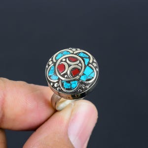 May include: A silver ring featuring a round turquoise and red stone inlay. The ring has a floral design and is set in a silver band.
