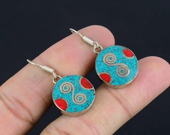 May include: A pair of round earrings with turquoise and red inlay. Each earring features a silver spiral design and a silver hook. The earrings are held in a hand against a dark background.