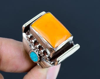 Könnte beinhalten: Ein silberner Ring mit einem orangefarbenen Edelstein und einem kleineren türkisfarbenen Stein. Der Ring hat ein detailliertes Design mit komplizierten Mustern.