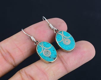 May include: Oval turquoise earrings with silver-colored metal accents. Each earring features a turquoise mosaic design with a silver spiral in the center. The earrings have a hook closure.