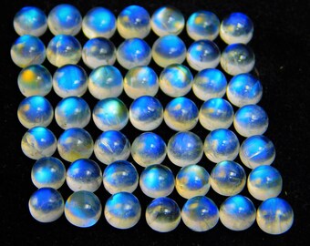 Op de afbeelding: Een verzameling ronde, gepolijste maansteen cabochons. Elke steen vertoont een melkachtige, doorschijnende uitstraling met een blauwe adularescentie en een subtiel kleurenspel. De stenen zijn dicht bij elkaar geplaatst tegen een donkere achtergrond.