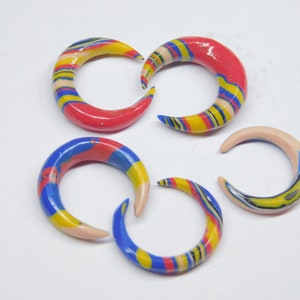 Peut inclure: Cinq boucles d'oreilles en forme de croissant en argile polymère, à rayures colorées. Les boucles d'oreilles sont dans les tons rouge, jaune, bleu et blanc.
