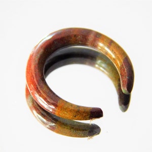 Peut inclure: Une paire de boucles d'oreilles créoles en céramique marron, verte et orange. Les créoles sont épaisses et ont une finition brillante.