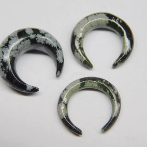 Peut inclure: Trois boucles d'oreilles en forme de croissant de lune en pierre noire et blanche. Les boucles d'oreilles ont un motif moucheté de noir, blanc et vert.