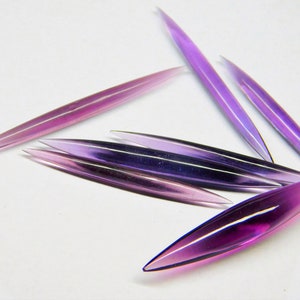 Peut inclure: Six tiges en verre violet avec des extrémités pointues. Les tiges sont disposées en éventail sur une surface blanche.