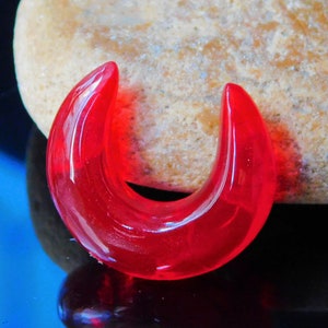 Peut inclure: Un jauge d'oreille en forme de fer à cheval en verre rouge vif. La jauge est lisse et brillante.