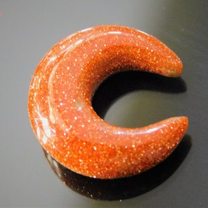 Peut inclure: Un bouchon d'oreille en forme de croissant, de couleur rouge-orange et scintillant.