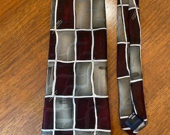 May include: A patterned necktie with a geometric design. The tie features a grid of burgundy, gray, and taupe squares, outlined with white lines. The tie is made in China.
