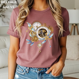 May include: Heather mauve t-shirt featuring a steampunk-inspired design. The design includes clocks, gears, a butterfly, and a dragonfly in shades of gold, blue, and white. The text "HEATHER MAUVE" is at the top of the image.