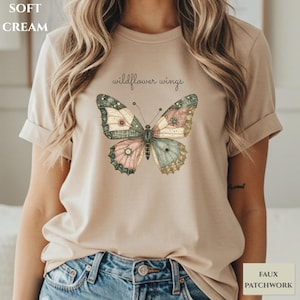 May include: A soft cream short-sleeve t-shirt featuring a central graphic of a butterfly with faux patchwork wings in muted tones of pink, blue, and green. The text "wildflower wings" is printed in a dark script font above the butterfly illustration.