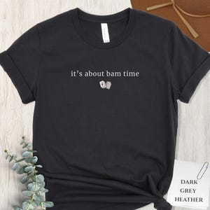 May include: Dark grey heather t-shirt with the text "it's about bam time" and a small graphic of two playing cards. The shirt has rolled-up sleeves and a classic crew neck.