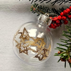 May include: A clear glass Christmas ornament with a gold lace design. The ornament is hanging from a silver cap with a diamond pattern.