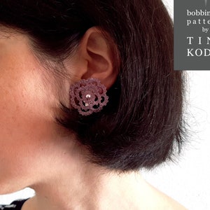 May include: A woman wearing a pair of pink bobbin lace earrings. The earrings are in the shape of a flower.