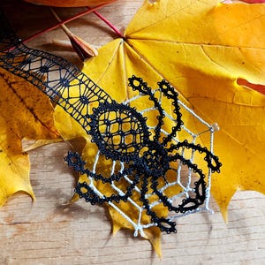 May include: A black and white lace spider on a yellow maple leaf, with an orange pumpkin and red and purple leaves in the background. The image includes the text "bobbin lace patterns by TINA KODER".
